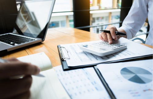 person sitting at desk with hand on calculator on top of tax forms